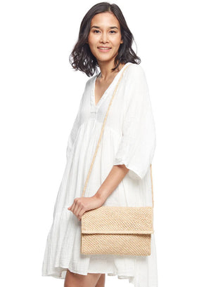 The MAR Y SOL - RHODES CROSSBODY CLUTCH from MAR Y SOL is a beige woven straw clutch bag featuring a tight, uniform weave that offers a natural, artisanal appearance. The simple yet elegant silhouette is adorned with delicate crochet detailing, making it perfect for both casual and semi-formal occasions.