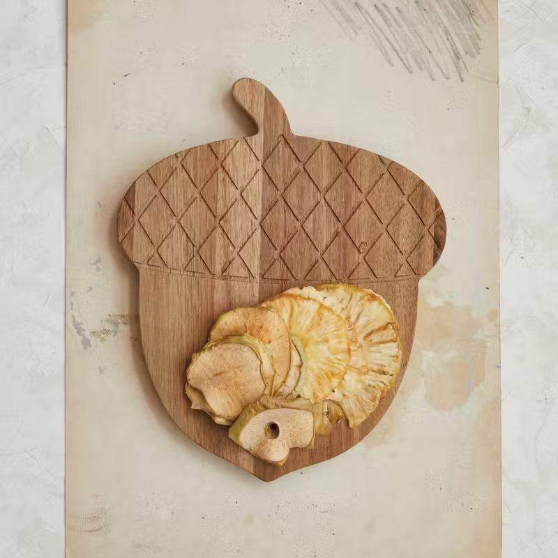 The ENGRAVED ACACIA WOOD ACORN CHEESE BOARD by CREATIVE COOP, fashioned from acacia wood, elegantly presents dried apple and pineapple slices on its textured surface. This food-safe piece adds a touch of rustic charm to any setting while ensuring both style and safety. To maintain its lasting beauty, remember that it's hand wash only.