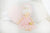 The ALIMROSE - CHARLOTTE DOLL PINK by ALIMROSE is a handcrafted doll with pale skin, dressed in a soft tulle light pink dress and carrying a golden purse. Her blonde hair is styled in a bun, and her small blue dot eyes coupled with a simple smile give her a charming expression.