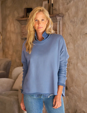 The FRANK & EILEEN ANNA Long Sleeve Capelet in Blueberry is showcased against a plain white background. This light blue, long-sleeve, crew-neck shirt boasts a relaxed fit and seamless hem, crafted from soft Triple Fleece. The slightly oversized design features the left sleeve casually folded at the cuff.