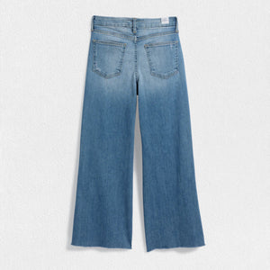 The FRANK & EILEEN Galway Gaucho Jean in the 1972 Wash offers a high-waisted, wide-leg design with a subtle faded effect and classic five-pocket styling, perfectly embodying the spirit of Italian Dream Denim. Featuring a raw hem for that iconic gaucho-style, these light blue jeans are showcased against a lightly textured background.