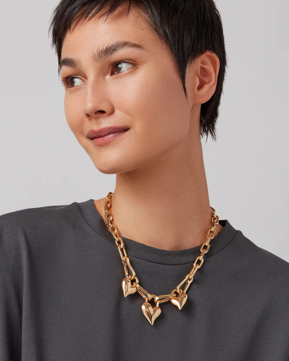 The JENNY BIRD Padlock Triple Heart Pendant Necklace features an elegantly elongated gold-tone dipped brass chain with three removable heart-shaped pendants, each evenly spaced. Its high-polish finish creates a stunning look against a plain white background.