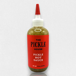 The product labeled "PICKLE HOUSE - PICKLE HOT SAUCE" from THE PICKLE HOUSE is displayed against a plain white background. The bottle, adorned with a red label featuring black text and capped with a white nozzle, contains 9.8oz (280g) of greenish-hued sauce. Its distinctive flavor arises from a secret spice blend mixed with tangy pickle brine.