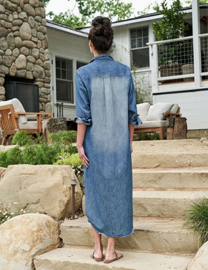 The FRANK & EILEEN Rory Maxi Shirtdress in Famous Denim is a full-length button-up dress featuring a collar, rolled-up sleeves to mid-length, and a single chest pocket. Its sleek, minimalist design embodies that California chic look against a plain white textured background.