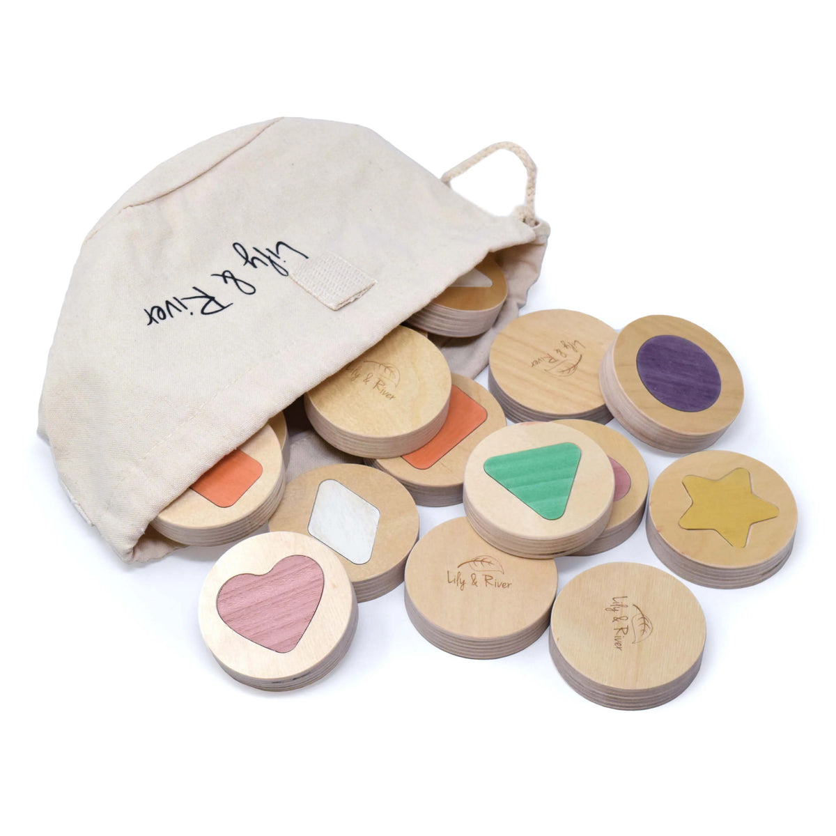 A young boy in a green shirt plays intently with the LITTLE MATCHABLES GAME SET by LILY &amp; RIVER on a white table in a Montessori playroom. The room is adorned with various toys and baskets, and the boy appears focused on enhancing his fine motor skills by arranging and stacking the round wooden discs as part of this engaging memory game.