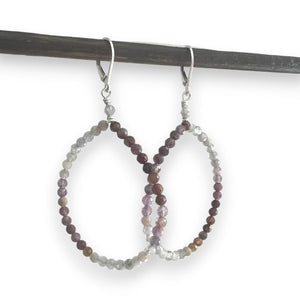 The ANN LIGHTFOOT - VARIED SPINEL HOOP EARRINGS showcase small, multicolored beads in hues of pink, purple, and orange. They hang gracefully from sterling silver earwires and are beautifully set against a dark gray background.