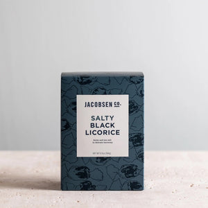 A blue box of Jacobsen Salt Co. Salty Black Licorice Box is placed against a neutral background. The box features a white label with black text and subtle black designs, highlighting its pure sea salt infused treat. The weight of the product is 5.5 oz (156 g).