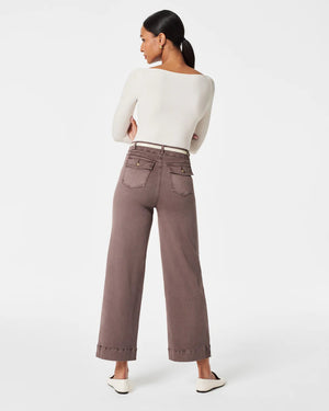 A woman stands confidently with her arms crossed, modeling a long-sleeve white top paired with high-waisted, wide-leg brown SPANX - STRETCH TWILL CROPPED PANTS. She completes the look with white slip-on shoes and is posed against a plain white background, gazing directly at the camera.