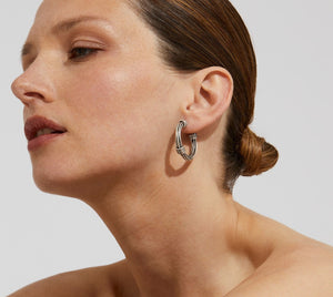 The GAS BIJOUX ARIANE SILVER HOOP EARRINGS are a stylish pair of silver hoops with a diameter of 2.7 cm, boasting a sleek and polished design accented by wrapped metallic threads at both the top and bottom. The reflective finish on the studs adds an elegant touch.