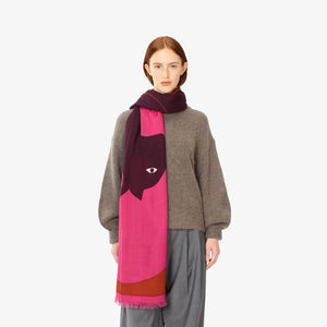 Close-up of a person wearing the INOUI EDITIONS - AMOUR SCARF in purple and pink cashmere, wrapped around their neck. The person has a neutral expression and is dressed in a grey sweater. The plain white background highlights the winter accessory from INOUI and part of the sweater.