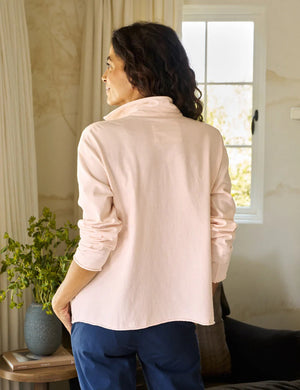 A person in a Frank & Eileen Patrick Popover Henley in Petal smiles with the collar popped, emphasizing the relaxed fit of the Heritage Jersey. The softly blurred background hints it's indoors.