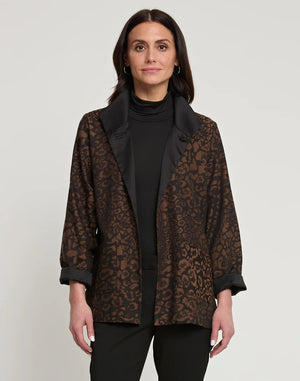 A woman with long dark hair is wearing the HINSON WU Constance Reversible Jacket, which features stylish leopard print details on the collar and belt. She pairs it with a black turtleneck top and pants while standing against a light background. The look balances style with practicality, as the jacket is conveniently machine washable.