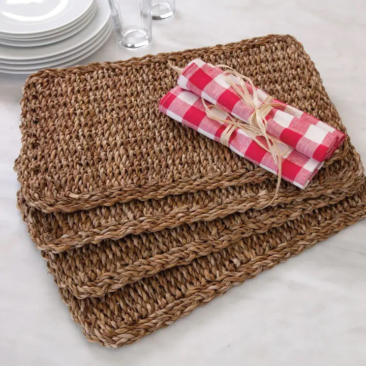 The SEAGRASS RECTANGULAR PLACEMAT by NAPA HOME AND GARDEN is crafted from brown seagrass fibers, featuring a rectangular shape with a coarse texture and visible loops. The edges are neatly finished, and the placemat is displayed on a plain white background.