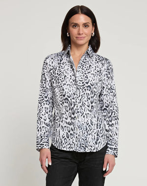 A person with long dark hair, wearing a fitted HINSON WU Diane Long Sleeve Snow Leopard Print Sateen Shirt in white and black, along with black pants, standing and facing the camera with a neutral expression. The background is plain light gray.