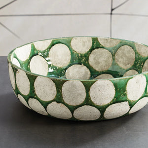 The NAPA HOME AND GARDEN - KILEY BOWL IN GREEN from NAPA HOME AND GARDEN is a ceramic piece with a green base and large gray circular patterns on a white background. It has a slightly rustic texture accented by a glossy finish, invoking mid-century pottery.