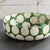 The NAPA HOME AND GARDEN - KILEY BOWL IN GREEN from NAPA HOME AND GARDEN is a ceramic piece with a green base and large gray circular patterns on a white background. It has a slightly rustic texture accented by a glossy finish, invoking mid-century pottery.