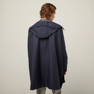 A person with short, wavy hair is seen from behind wearing the TILLEY - PACKABLE HOODED PONCHO by TILLEY in dark navy, featuring a hood and a loose, water-repellent fit, set against a plain light background.