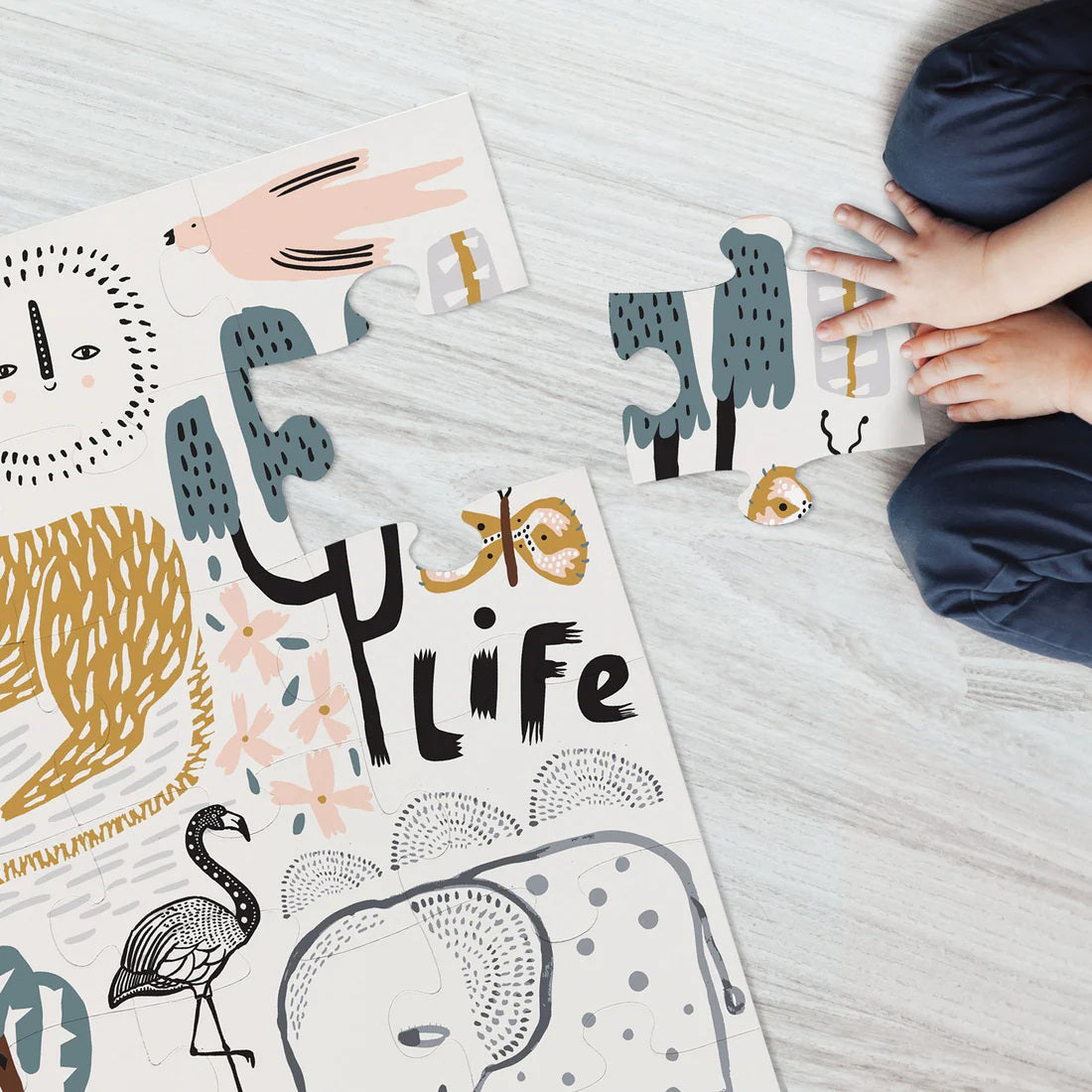 Presenting the WEE GALLERY - WILD LIFE FLOOR PUZZLE by WEE GALLERY—this large floor puzzle features whimsical wildlife illustrations, showcasing a lion, elephant, giraffe, monkeys, flamingo, and various trees. Made from eco-friendly materials and designed for ages 3 and up, it contains 24 pieces that promote motor skill development. The text on the puzzle reads &quot;Wild Life&quot; and &quot;large floor puzzle.