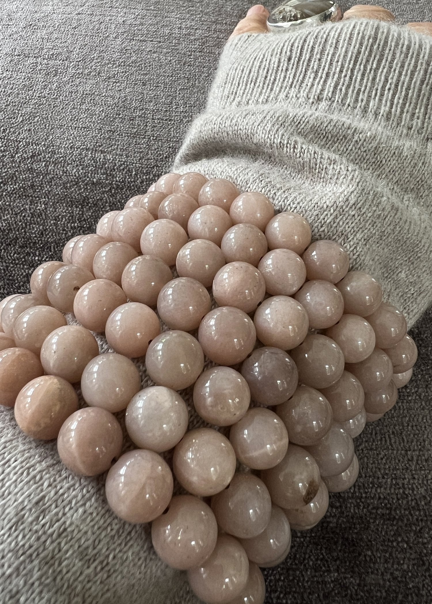 The ANN LIGHTFOOT - Pink Moonstone Elastic Cuff Bracelet comprises a coiled strand of 10mm beads, gracefully arranged on a white surface. These polished moonstone beads feature a smooth, glossy finish, showcasing subtle variations in color and semi-translucence.