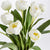 A no-maintenance arrangement featuring the PEONY TULIP DROP IN 18 by NAPA HOME AND GARDEN, showcasing a bouquet of white tulips with lush green leaves, elegantly tied with natural jute twine against a plain white background.