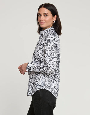 A person with long dark hair, wearing a fitted HINSON WU Diane Long Sleeve Snow Leopard Print Sateen Shirt in white and black, along with black pants, standing and facing the camera with a neutral expression. The background is plain light gray.