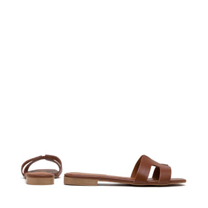 The image depicts the MICHELE LOPRIORE - H SLIDE, a single brown leather slide sandal with an open-toe design. The upper features two wide straps with geometric cutouts. The thin sole appears to be made of light brown wood-like material. Made in Italy by MICHELE LOPRIORE, the sandal is displayed against a plain white background.