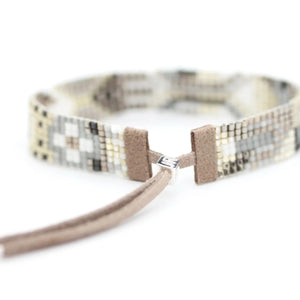 Introducing the JULIE ROFMAN - OSLO BRACELET by JULIE ROFMAN JEWELRY: A beaded bracelet that boasts a captivating geometric design in beige, gray, and brown hues. It features a stylish leather strap with a metallic clasp at the centerpiece and an adjustable closure to ensure the perfect fit.