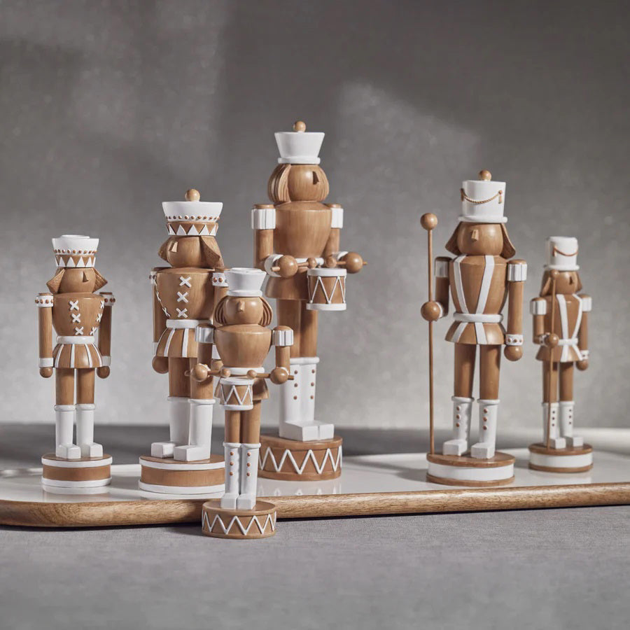 A collection of ZODAX's decorative nutcrackers, featuring various sizes and styles, is elegantly displayed on a wooden platform. The elaborate white details and accessories such as drums, scepters, and hats enhance their charm against the delicate gray backdrop.