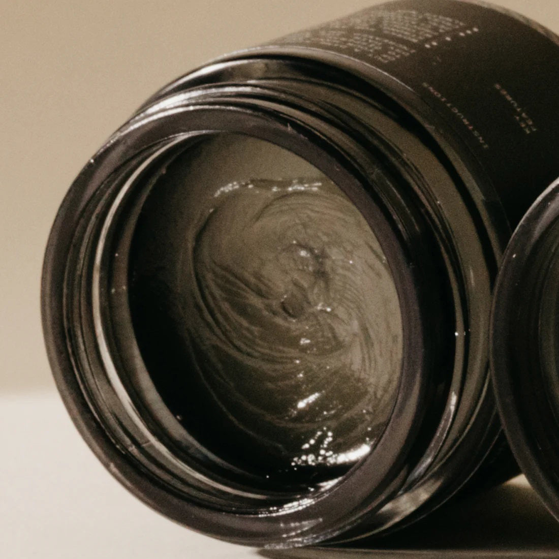 A small, black jar labeled &quot;PRESTON - WET WAX&quot; stands against a plain, beige background. Light and shadow create a soft, minimalist aesthetic around the jar, emphasizing its simple and elegant design. This cruelty-free medium shine product is a firm hold styling aid perfect for sleek finishes.