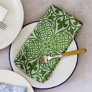 A VIETRI white plate with a blue rim holds a VIETRI DAMASK NAPKIN, made from 100% cotton, intricately patterned beside a silver fork with a wooden handle. Elegant table decor is created by surrounding it with other plates on the light gray surface.