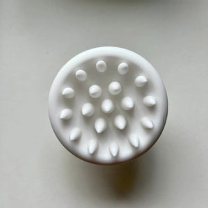 A white, round door knob with a smooth, oval-shaped handle is centered in the image against a plain, light-colored background. The unmarked handle appears clean and unadorned, reminiscent of the sleek design of the SCALP MASSAGING BRUSH by INDEX BY DEX.