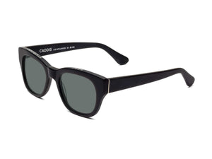 A pair of CADDIS - MIKLOS SUNGLASSES in matte black, featuring a premium bio-based acetate frame and grey polarized lenses, positioned at an angle to showcase the inside arm with the visible CADDIS brand name.