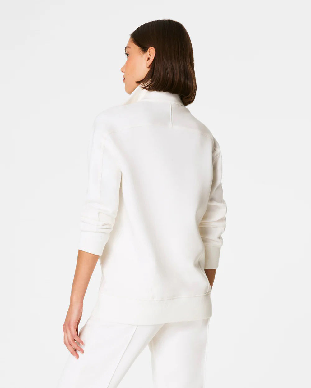 A person with shoulder-length hair faces away from the camera, showcasing the SPANX - AIRESSENTIALS LUXE HALF ZIP TUNIC in super-soft spacer fabric. This set offers bum coverage and blends style with comfort against a plain white background.