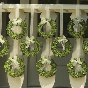 The BOXWOOD WREATH by NAPA HOME AND GARDEN features preserved English boxwood leaves in a compact green design. Adorned with a sheer white ribbon tied into a bow at the top and hung by a longer sheer white ribbon, this elegant piece of home decor is perfect for indoor use.