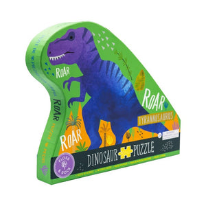 A vibrant dinosaur puzzle box shaped like a green dinosaur showcases a roaring blue and purple Tyrannosaurus. The box features labels reading "ROAR" and "Dinosaur Puzzle," contains 40 chunky puzzle pieces, and is branded by Floss & Rock.