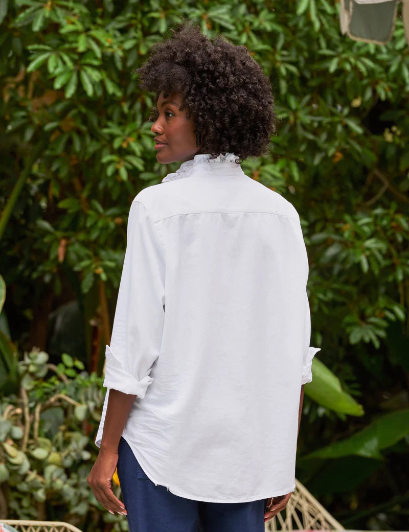 The FRANK &amp; EILEEN Ruffle Eileen Ruffle Collar Button Up Shirt in White Famous Denim features rolled-up long sleeves, a ruffled collar, and a single chest pocket, shown against a white background.