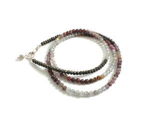 The ANN LIGHTFOOT - TRIPLE WRAP VARIEGATED SPINEL BRACELET features small, faceted spinel beads in a range of colors, including shades of gray, pink, brown, and beige. Coiled neatly on a dark background, the beads add a subtle shine to this elegant piece.