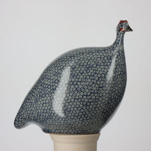 The LES CERAMIQUES DE LUSSAN - LARGE PECKING CERAMIC FRENCH GUINEA IN BLUE SPOTTED COBALT sculpture showcases a pattern of small blue circles on a white background. It is elegantly displayed on a simple, light-colored pedestal against a neutral backdrop, reflecting the artistry of traditional ceramic workshops.