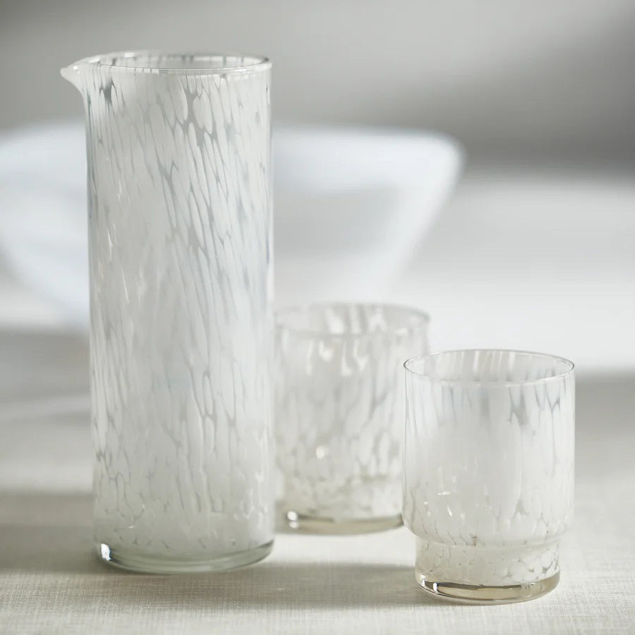 Presenting the AMALFI WHITE TORTOISE PITCHER by ZODAX: a tall, cylindrical clear glass pitcher with a small spout on one side. With a capacity of 946 ml (32 oz), this elegant piece features a textured, marbled pattern and boasts an elegantly simple design.