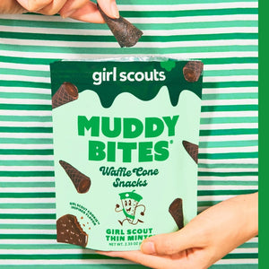 Image of a MUDDY BITES- THIN MINT WAFFLE CONES product package. The green package emphasizes the Girl Scout Thin Mints flavor, featuring mini waffle cones filled with mint chocolate and dark chocolate. It also showcases nutrition facts, GMO-Free and Kosher certifications, and resealable packaging for freshness. Founders: Jared and Tyler.