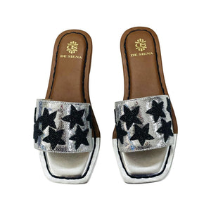 Introducing the DA SIENA – BEADED STARS SLIDES by DE SIENA. These open-toe leather slides feature brown soles and exquisite gold detailing. The straps are elegantly adorned with black beaded stars, while the cushioned insole in light brown showcases the DE SIENA logo and name. The sandals boast a chic flat, rectangular design.