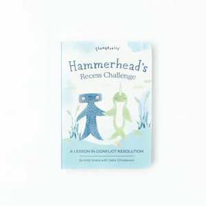 A child's hand points at a page of the SLUMBERKINS - RECESS CHALLENGE BOOK by SLUMBERKINS. The page features illustrations of underwater creatures, including a blue octopus, a turtle, and a fish, accompanied by text about a hummingbird who gains the courage to fly using calming techniques. The background of the book is white with soft colors.