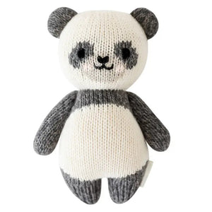 Introducing the CUDDLE + KIND - HANDMADE BABY PANDA from CUDDLE & KIND, a charming, hand-knit plush toy featuring gray ears, arms, and legs, and a white body accented with gray around the eyes and limbs. The panda's smiling face and black eyes add to its adorable appeal. This lovely toy is perfect for baby shower gifts, crafted with love to support fair trade income initiatives.