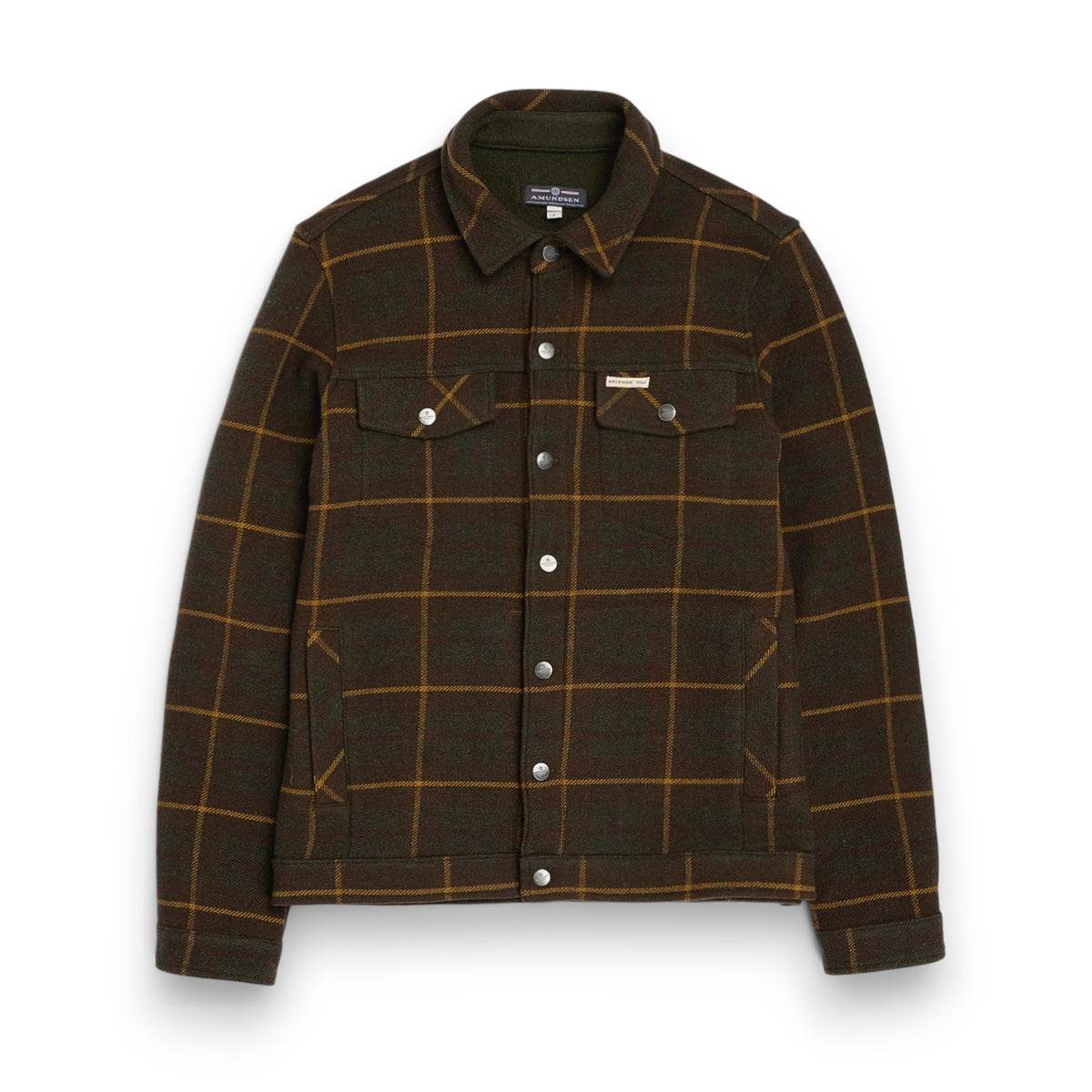 The AMUNDSEN SPORTS Wool Jacket is a unisex dark plaid overshirt with a brown and mustard check pattern, long sleeves, buttoned cuffs, and a small red, white, and blue striped tag near the back collar. Laid flat, viewed from behind.