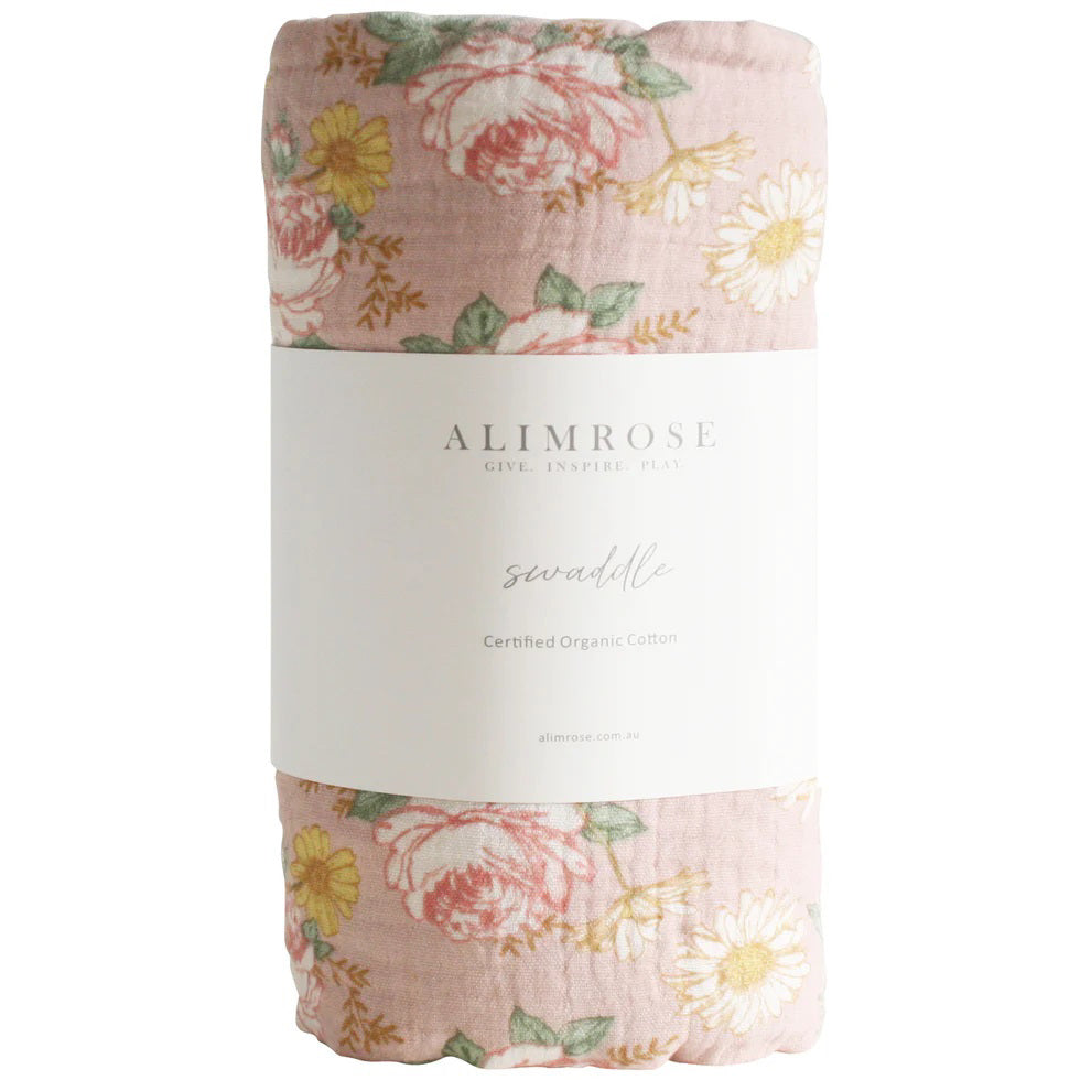 An ALIMROSE Muslin Swaddle made from 100% organic cotton. The pink swaddle features a charming pattern of white daisies, and the label includes the brand name and product details. It's conveniently machine washable.