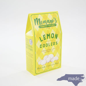 A yellow and green diamond-patterned box labeled "MEMAWS COUNTRY KITCHEN - LEMON COOLERS" from the brand 1 IN 6 SNACKS is pictured. The box displays images of sweet and zesty lemon cookies dusted with sugar. A blue silhouette of North Carolina with the word "made." is in the bottom right corner.