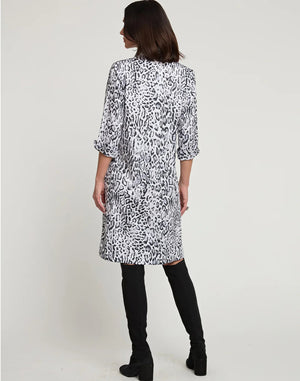 A woman with shoulder-length dark hair is wearing a knee-length HINSON WU - CHARLOTTE 3/4 Sleeve Snow Leopard Sateen Dress. She is also sporting black knee-high boots and has her hands in the dress pockets. The background is plain white.