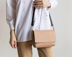 A person in an olive green trench coat holds the WOOLBERRY WOOL FELT CROSSBODY BAG in light gray with a black strap; only their torso and hand are visible.