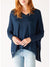 A person with long, reddish hair is wearing the MERSEA - CATALINA V NECK SWEATER from MER SEA, featuring its signature split sides that add a touch of flair. Paired with light blue jeans, this year-round closet hero stands in front of a plain background, their hands together resting just below the waist.