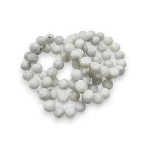 A string of round grey beads, possibly made of agate, arranged in a spiraled pattern against a plain white background, reminiscent of the elegant ANN LIGHTFOOT - GREY AGATE STRETCH BRACELET by ANN LIGHTFOOT.